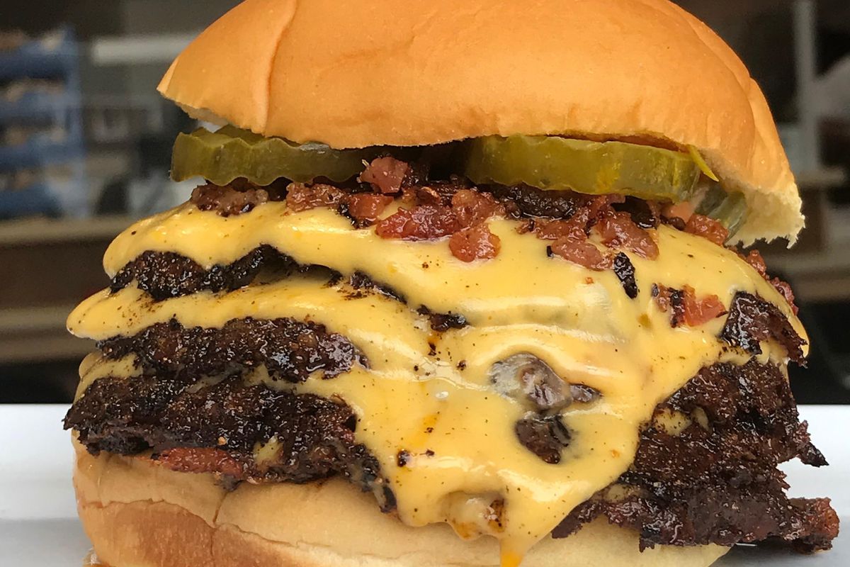 A triple cheese burger with bacon bits and dill pickles