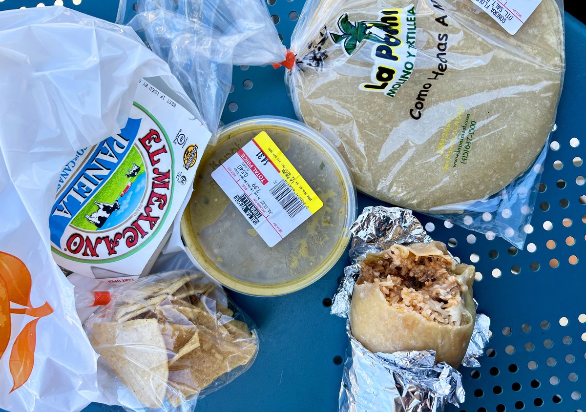 A burrito, salsa, and a bag or tortillas on a table.