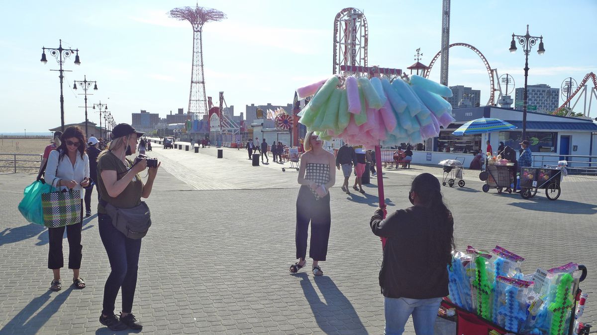 A boardwalk with a verdor holding up a pole of bags of pastel cotton candy.