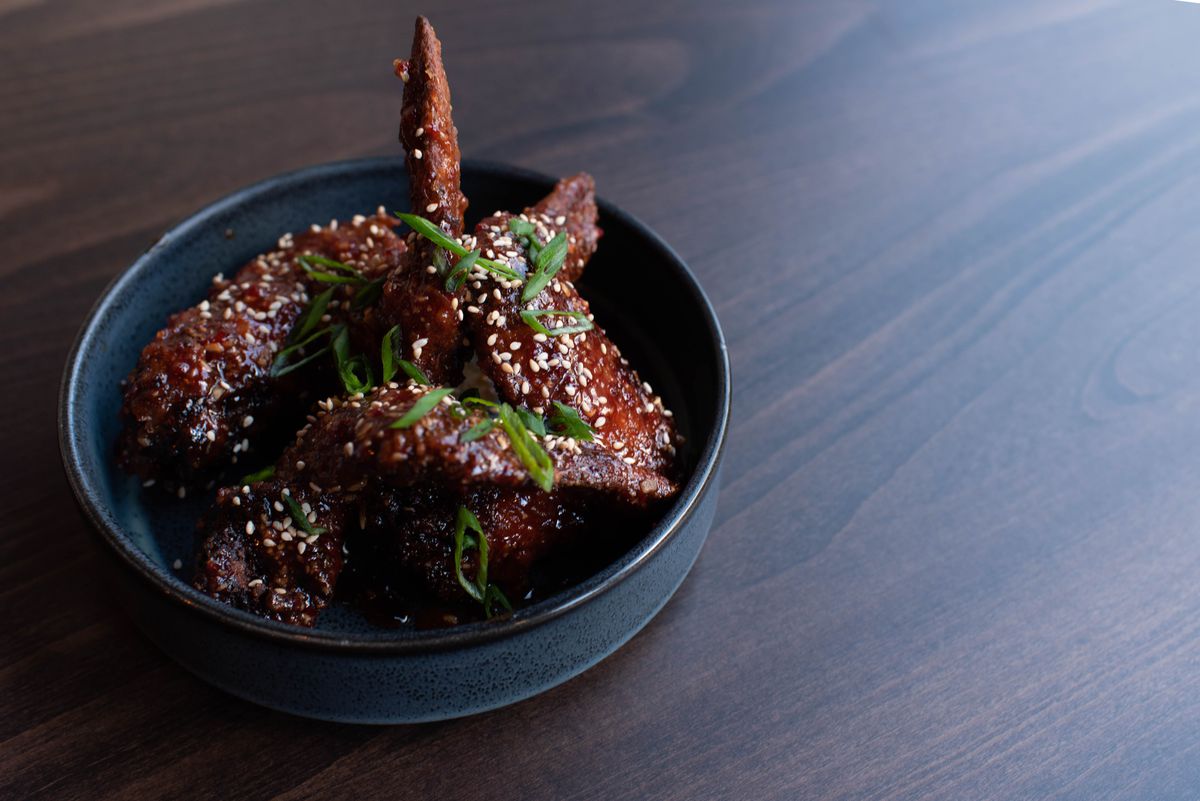 Red-brown sauce-covered chicken wings sprinkled with sliced scallions and sesame seeds in a blue ceramic bowl.