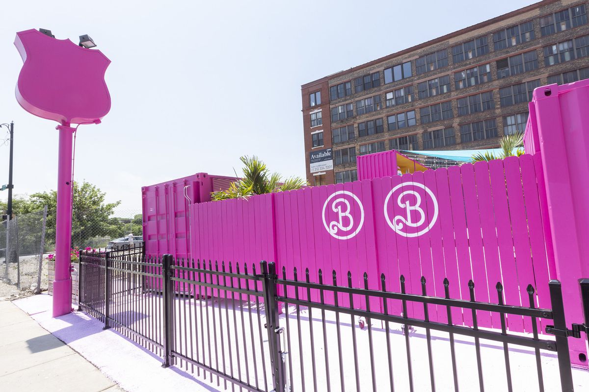 A very tall sign and fence are painted bright pink with a white “B” logo stenciled on the fence.