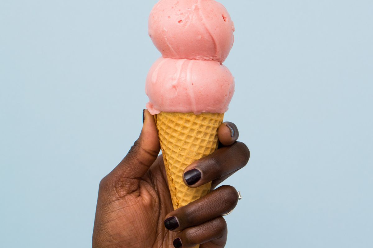 一个黑人的手拿着一个在蓝色背景下的粉红色冰淇淋的华夫蛋筒