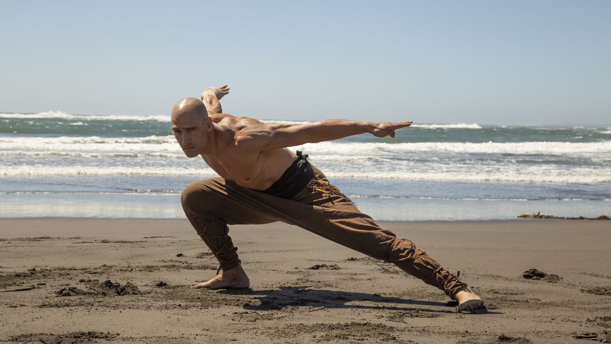 Marko Zaror crouches low in a defensive pose on a beach in Fist of the Condor, with the ocean behind him.