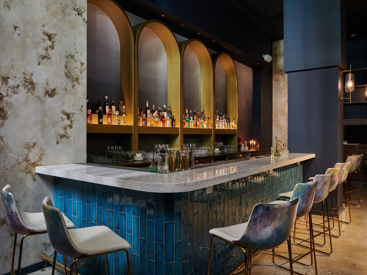 A bar with a marble top, high chairs, and a bar in the background.