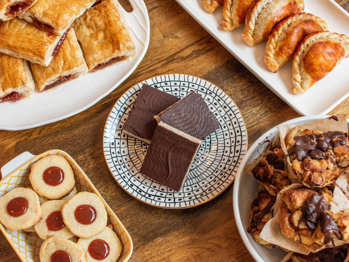 Empanadas, guava-stuffed pastelitos, and other dishes sit on decorative plates on a wood table.