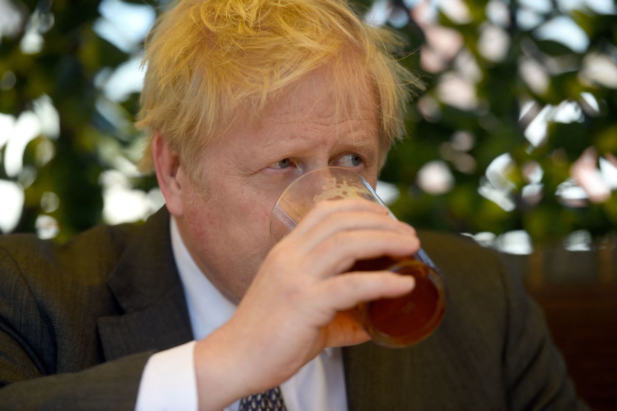 Boris Johnson sits drinking a pint of beer while wearing a suit