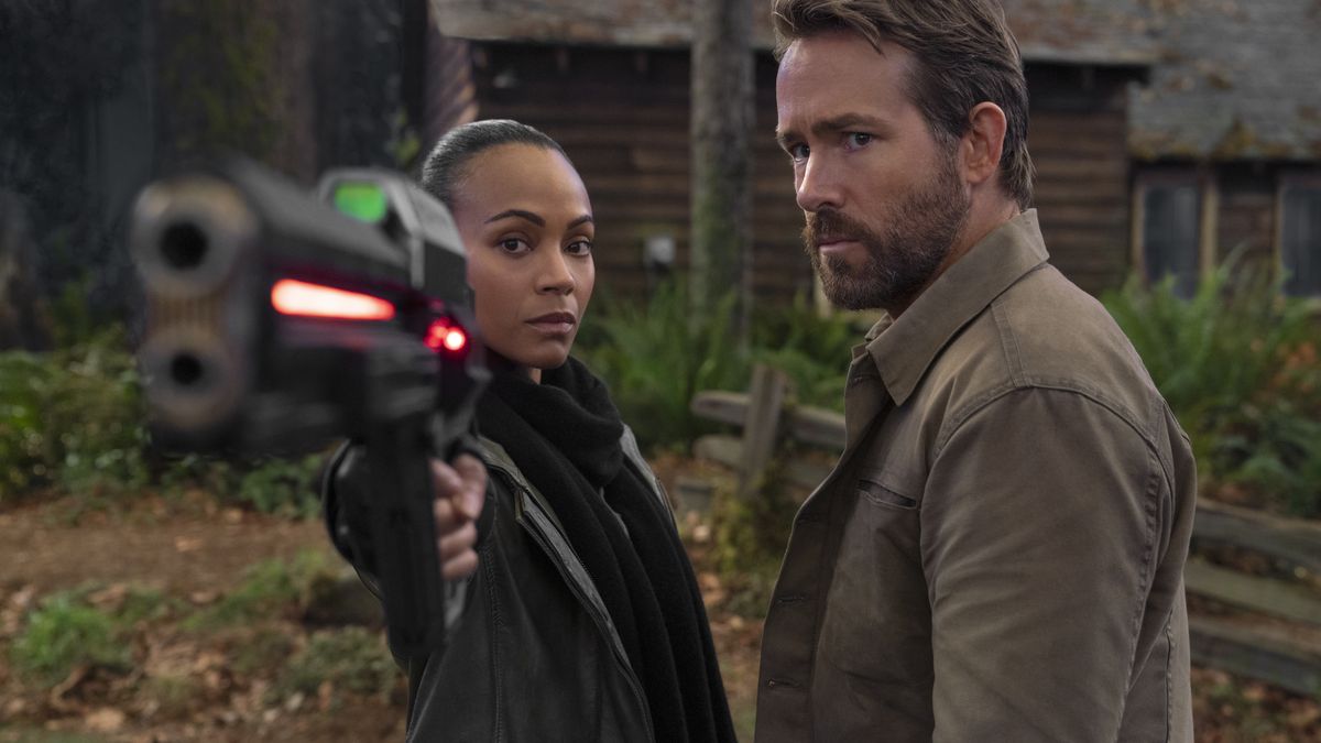 Zoe Saldana and Ryan Reynolds stand side by side outdoors in The Adam Project, with Zoe pointing a giant-ass glowing futuristic gun at the camera