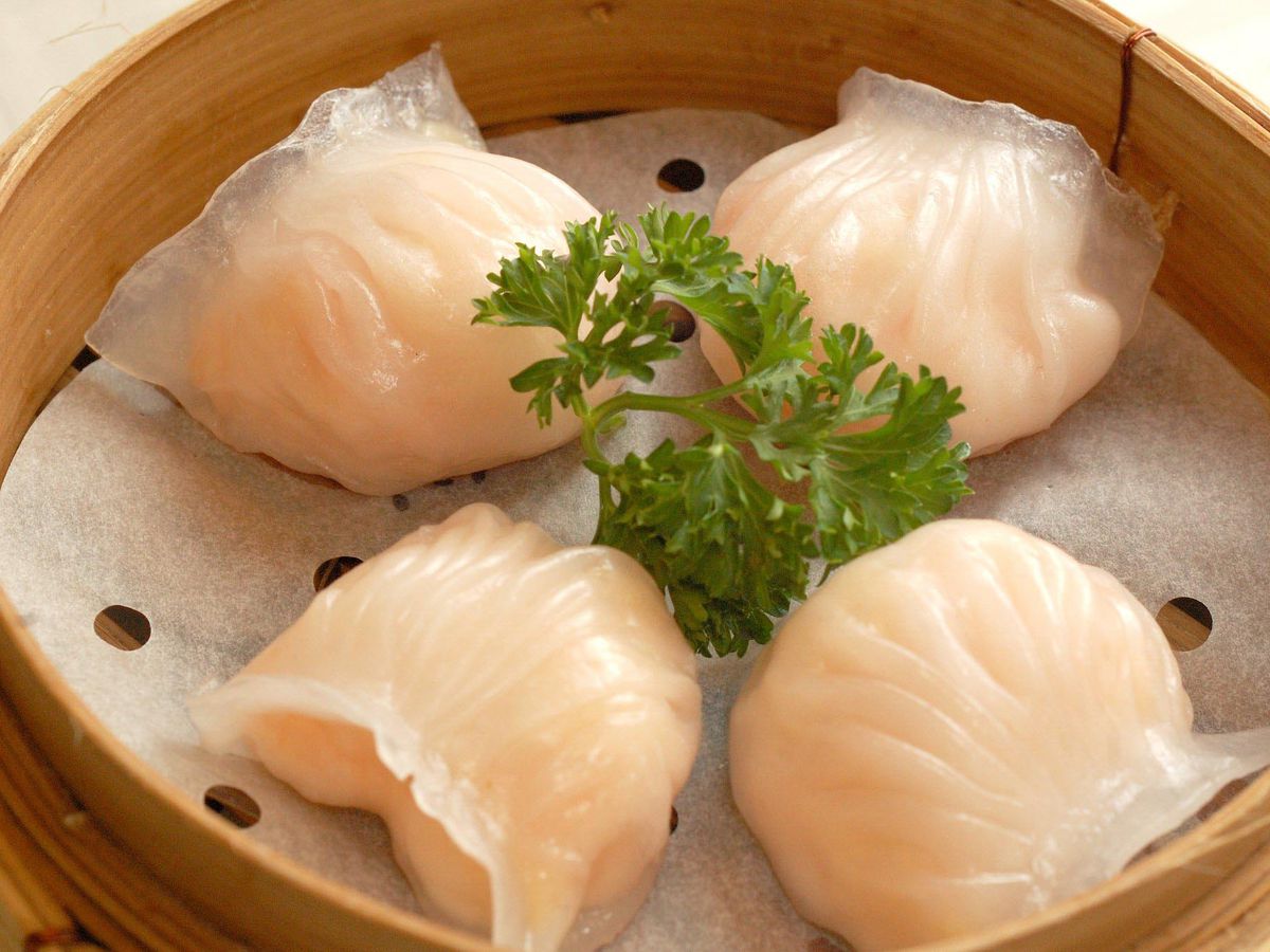 Four shrimp dumplings in a bamboo steamer with a sprig of parsley in the middle.