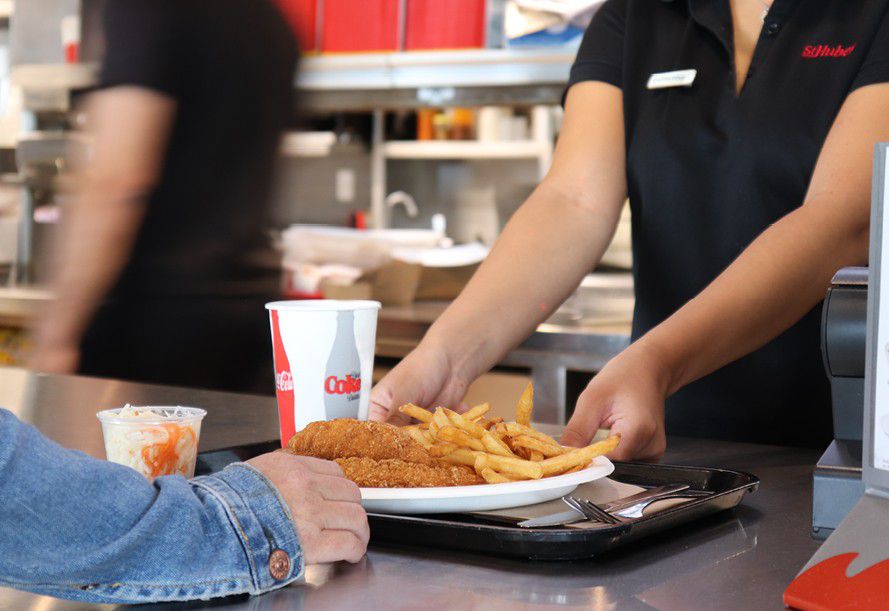 A worker handing chicken fingers and fries to a customer.