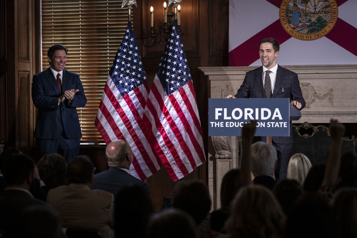 DeSantis laughs and applauds as Rufo speaks at a lectern reading “Florida: The Education State.”
