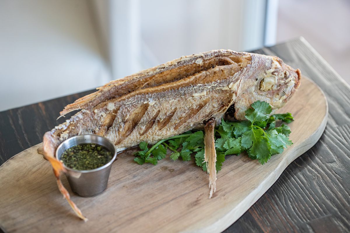 Whole fried fish on a wooden plank with herb fish sauce.