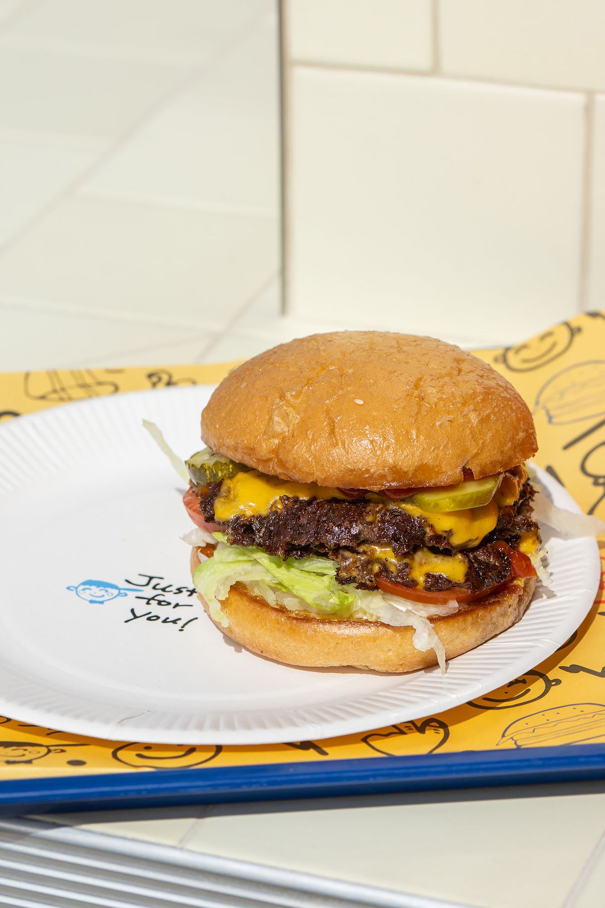 A tilted bright shot of a tall two-patty burger on a white plate and blue tray.