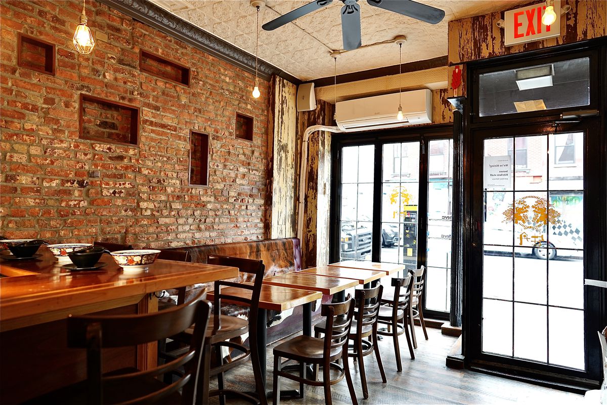 Inside a small restaurant with exposed red brick walls, glass windows with panels and a set of wooden chairs and tables