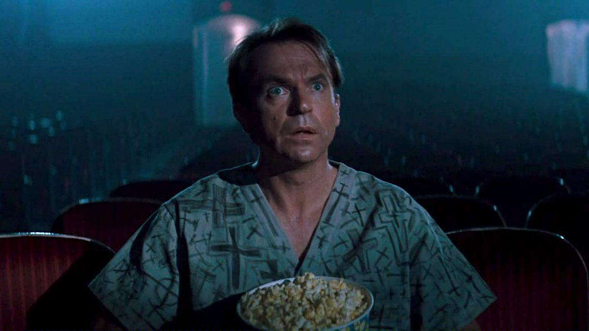 Sam Neill, sitting in a movie theater alone with a tub of popcorn, gapes at the screen in awe in the movie In the Mouth of Madness