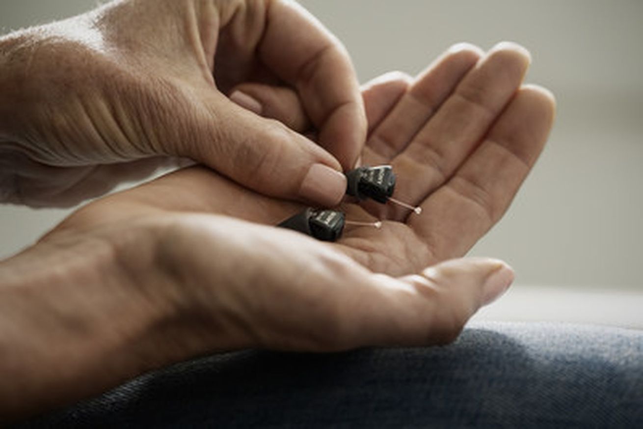 Small hearing aids held in an outstretched hand.