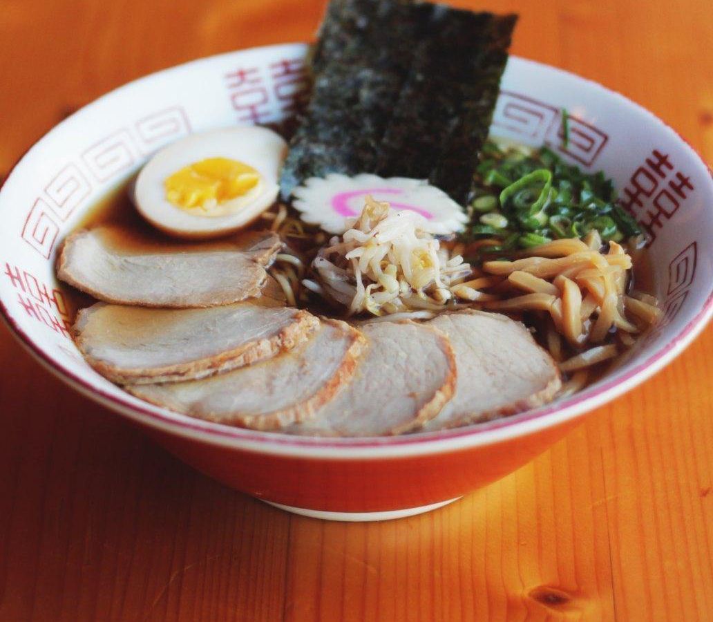 A bowl of ramen topped with pale slices of meat, a boiled egg, vegetables, and seaweed.