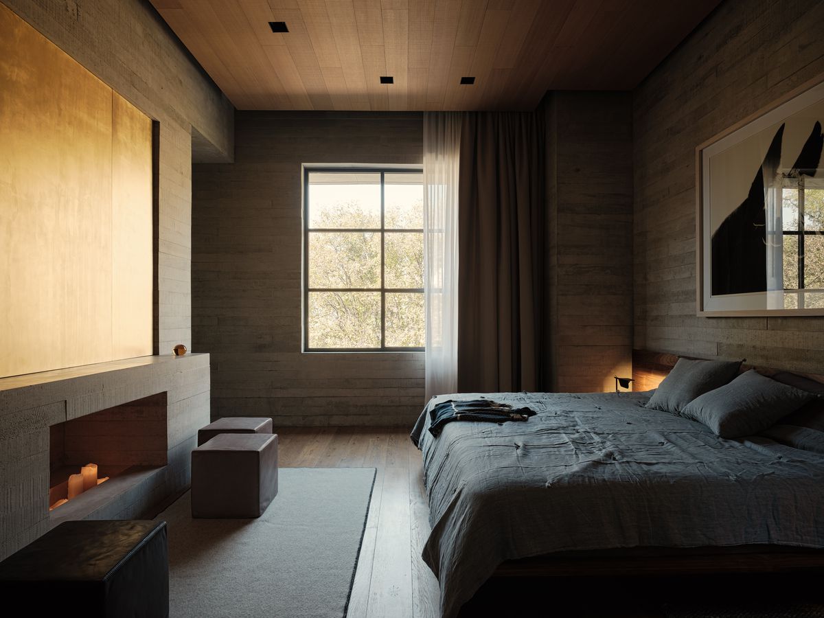 Bedroom with a large gridded window, fireplace, and bed with gray sheets. 