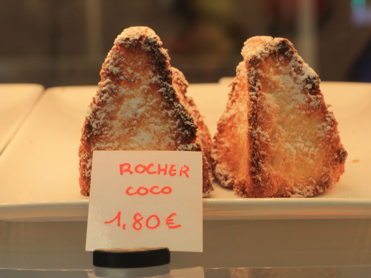 Sugar-covered macaroons in a pastry case with a handwritten sign reading ‘rocher coco’
