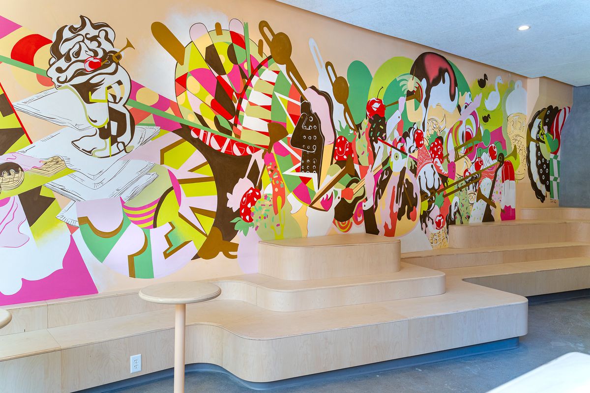 A colorful mural on a long wall behind wooden bleachers and two small tables.