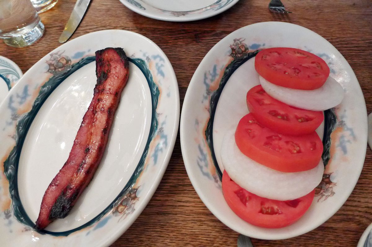 On one plate one slice of bacon, on the other sliced tomatoes and onions.