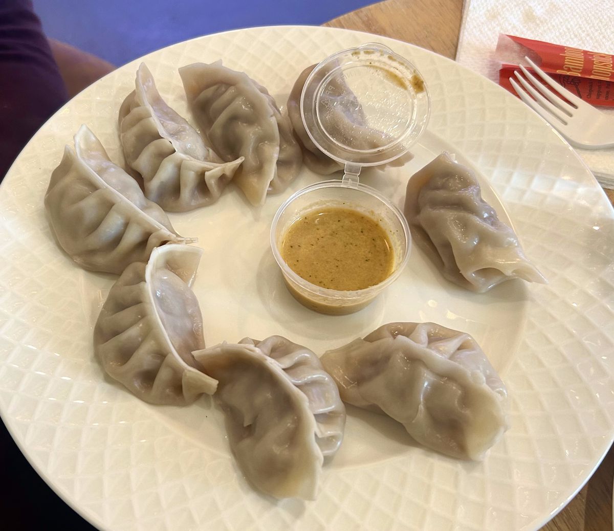 Eight momos arranged on a plate around a dipping sauce.