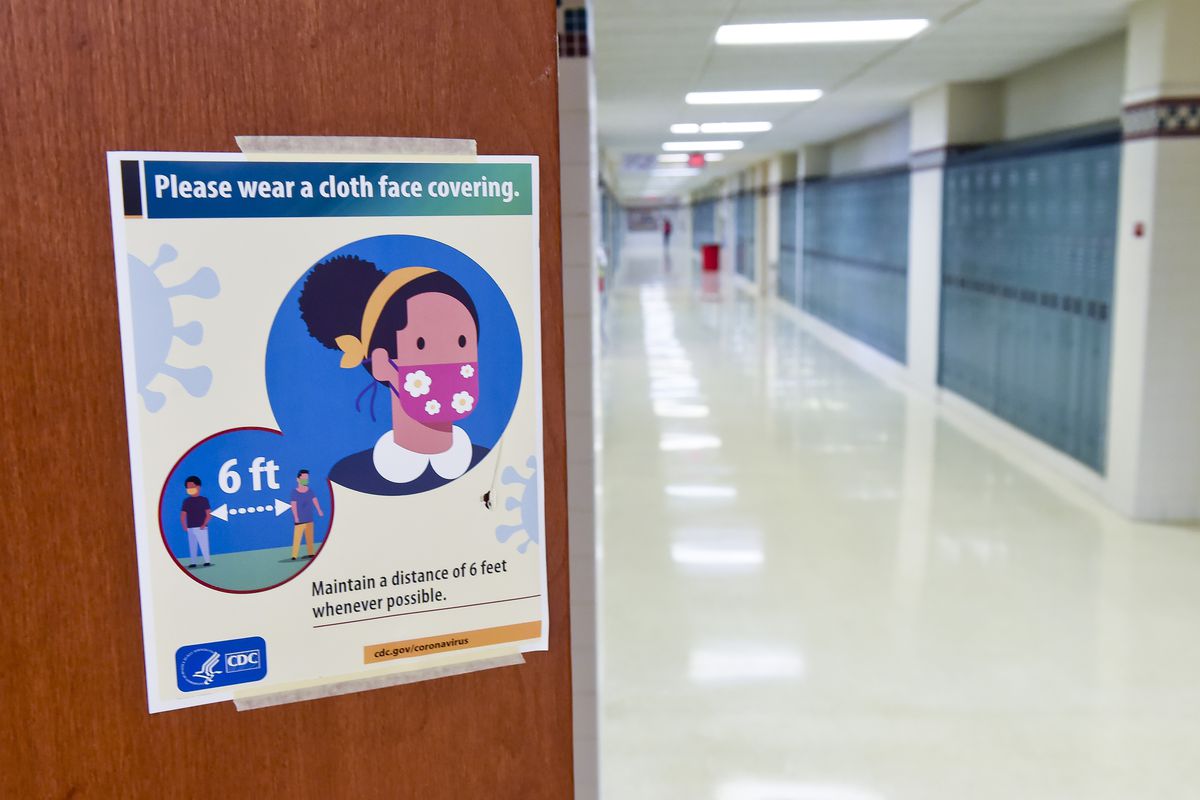 A CDC poster in an empty school hallway reads, “Please wear a cloth face covering.”