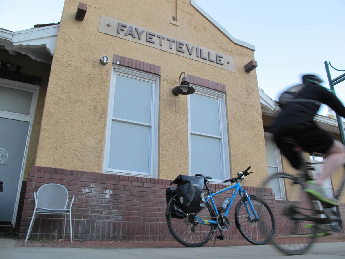 A bike loaded with two bags above its rear tire rest against an old depot building in Fayetteville, Arkansas. 