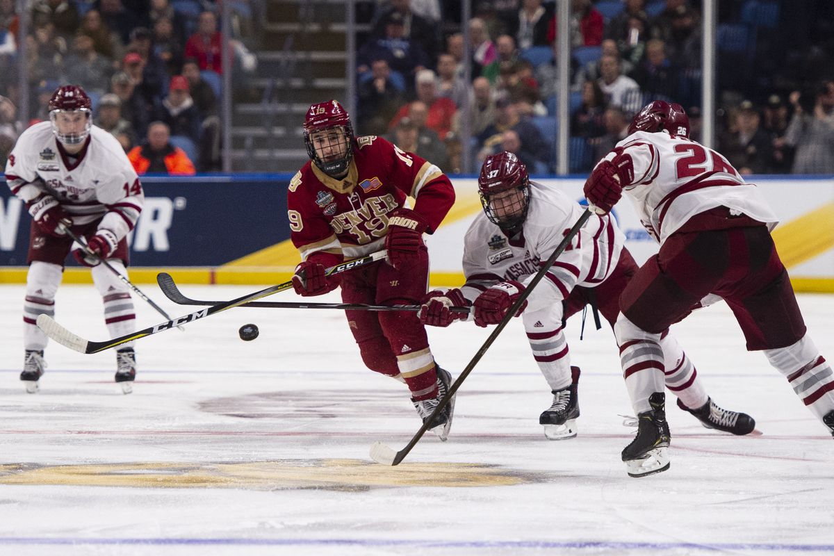 Denver Pioneers Forward Cole Guttman (19) shoots the puck with Massachusetts Minutemen Forward Phillip Lagunov (17) and Massachusetts Minutemen Defenseman Colin Felix (26) defending during the second period of the NCAA Hockey Frozen Four semi-final game between the Massachusetts Minutemen and the Denver Pioneers on April 11, 2019, at the Key Bank Center in Buffalo, NY.