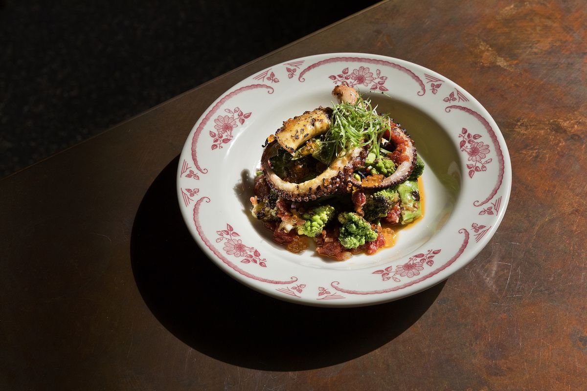 A vintage bowl holds grilled octopus tendrils in shadowy light at a restaurant.