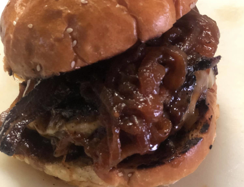 A closeup of a burger smothered in barbecue sauce and onions