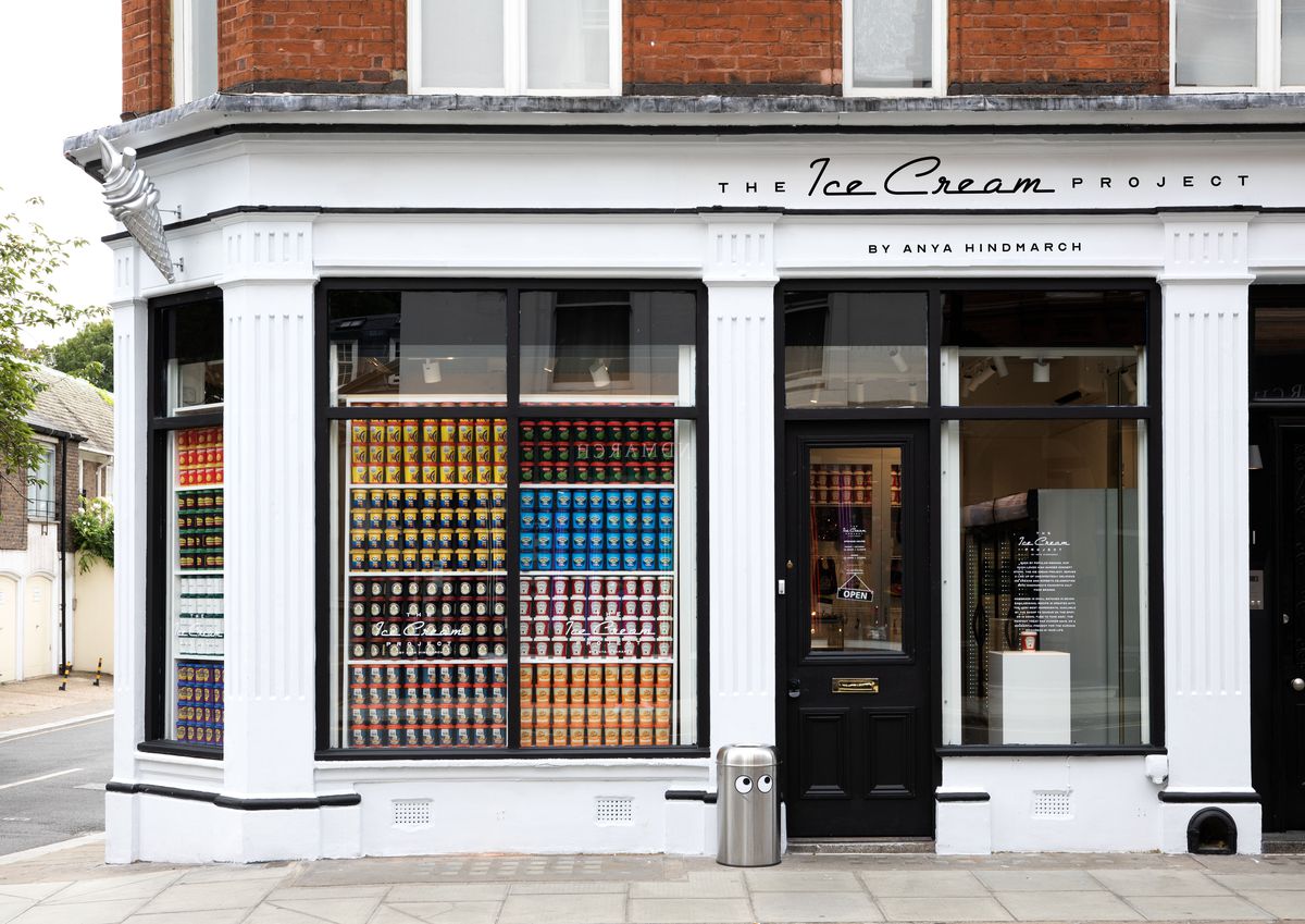 A white store exterior with large windows showing off pints of ice cream stacked in tall towers, with The Ice Cream Project written above the door. 