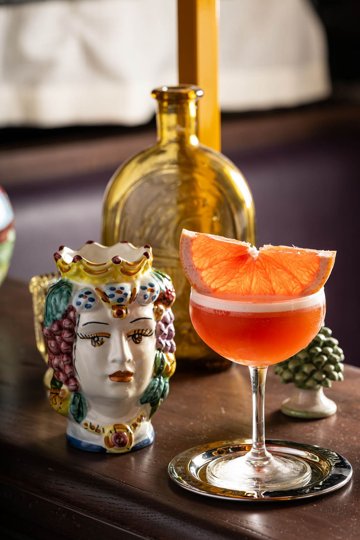 An orange-colored cocktail with a grapefruit slice next to a ceramic doll at Donna’s restaurant.