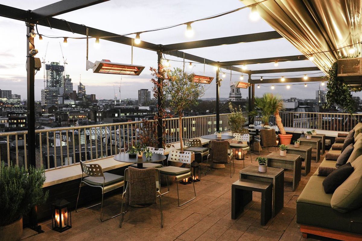 A hotel rooftop in Shoreditch adorned with filament bulbs, cushioned seating, and wooden decking