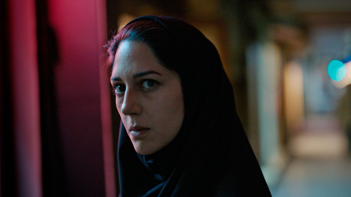 A woman (Zar Amir Ebrahimi) wearing a head scarf and standing in a darkened alleyway at night.
