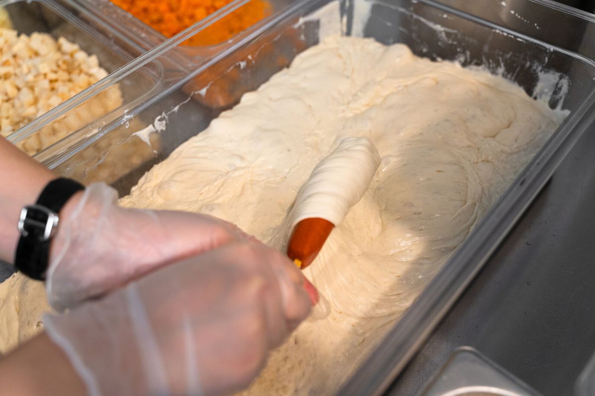A worker dips a hot dog on a stick in a tray of batter