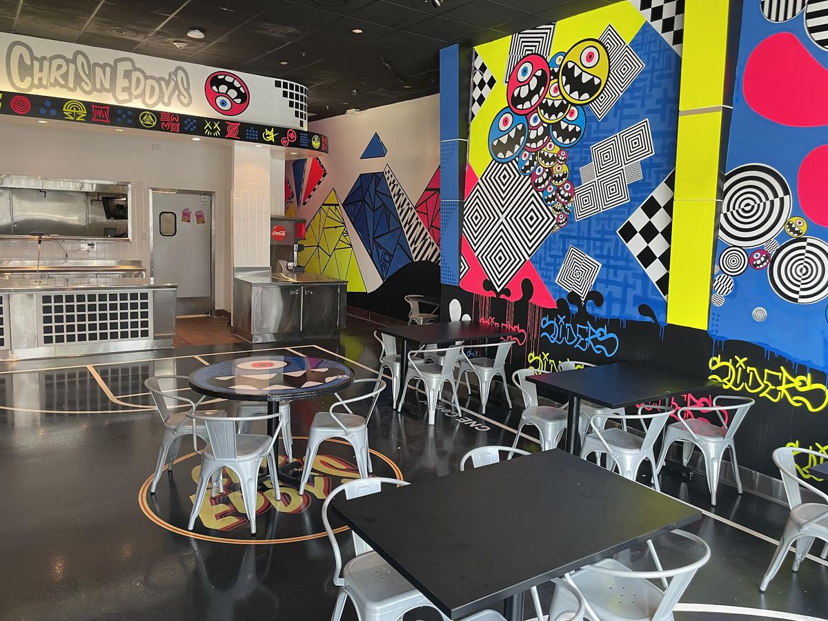 A neon and wildly-designed restaurant with funky art on the walls and metal chairs.