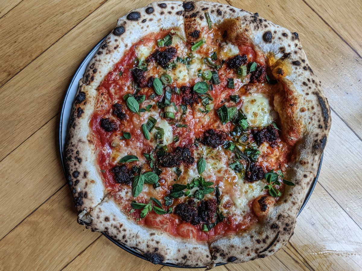 A full pizza topped with nduja and herbs, shot from above on a wood table