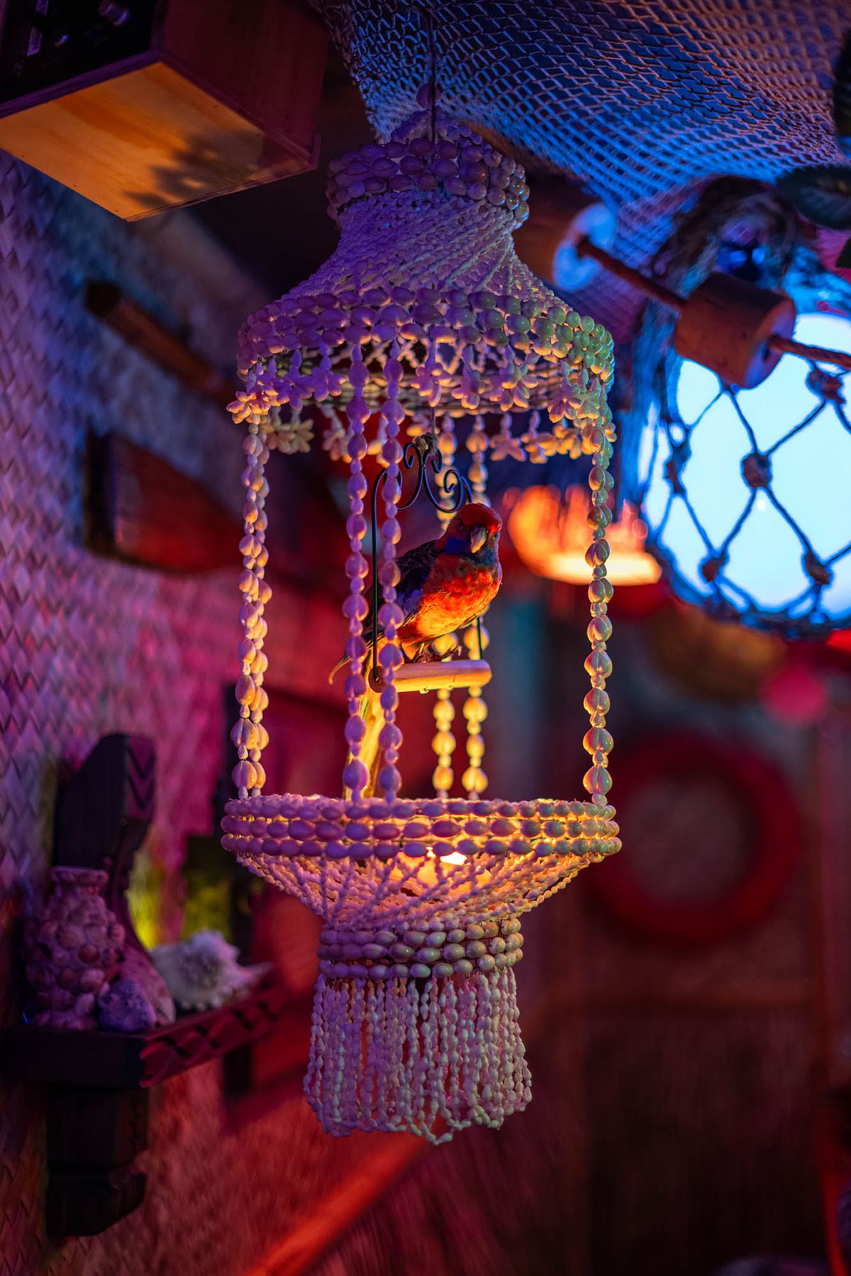 A fake bird inside of a woven pot holder hanging from a ceiling inside of a dark, colorful underground tiki bar named Tiki Mirage in Los Angeles.