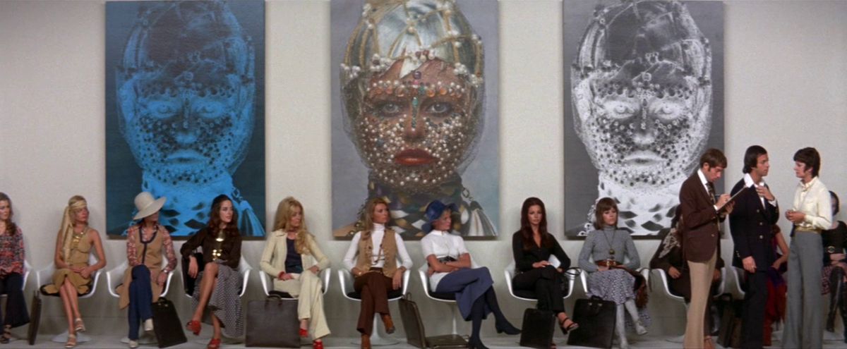 A group of women, including Jane Fonda, sit in a line in front of three paintings.