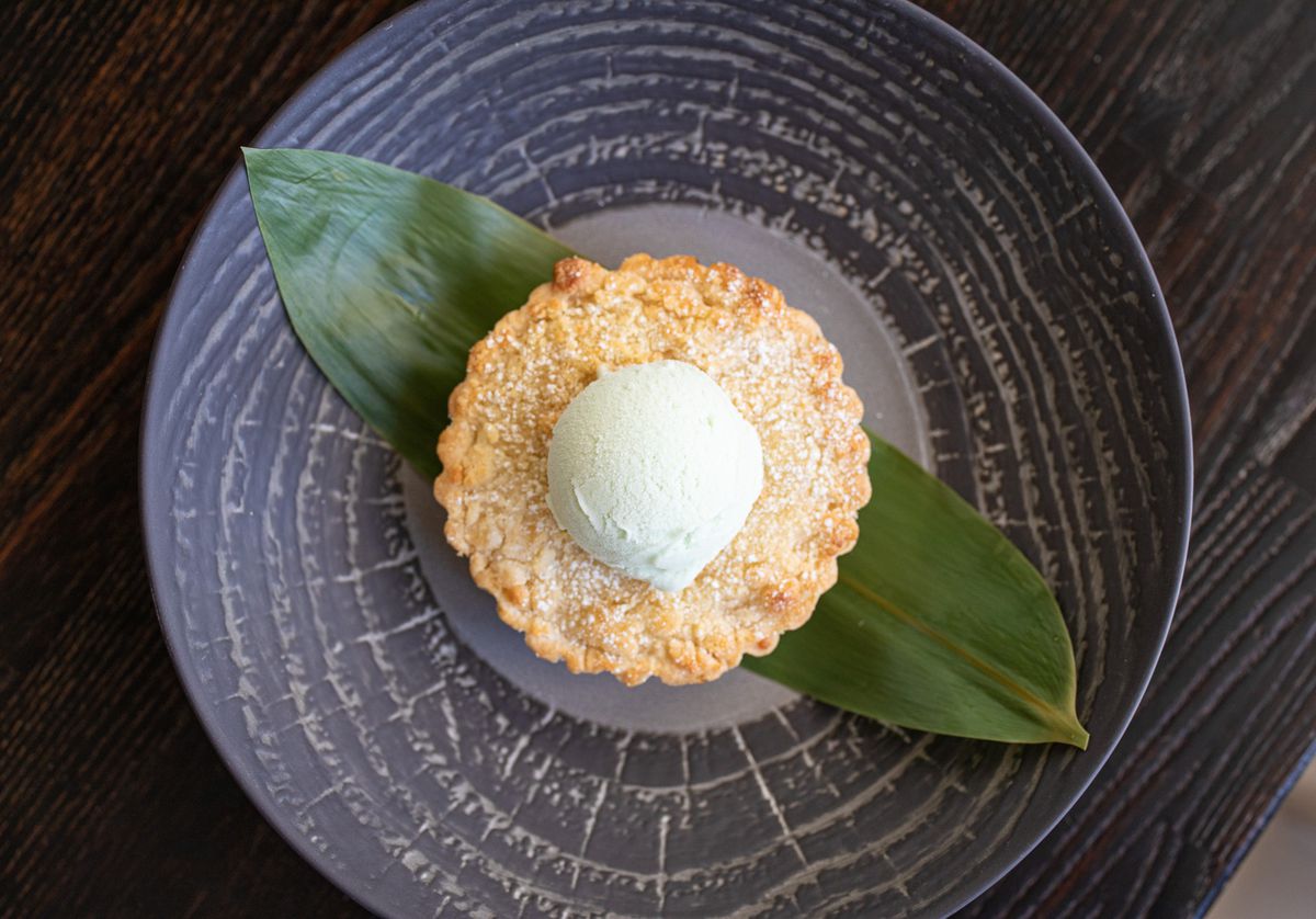 Young coconut tart with coconut pandan ice cream on a dark textured plate.