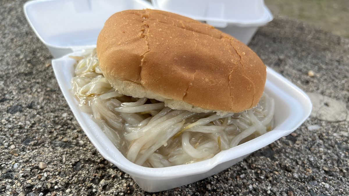 A pile of bean sprouts in a cornstarchy gravy sits on a hamburger bun in a small white styrofoam container.