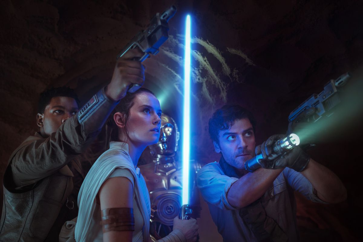 Finn aiming his gun upward, Rey holding her blue lightsaber straight upward, and Poe aiming a gun and flashlight upward, with C-3PO standing behind them, in Star Wars: The Rise of Skywalker