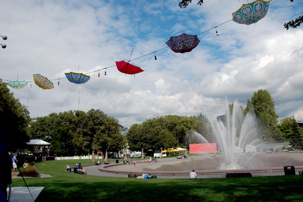 A row of upside down umbrellas mounted on a wire above a lawn and large fountain.