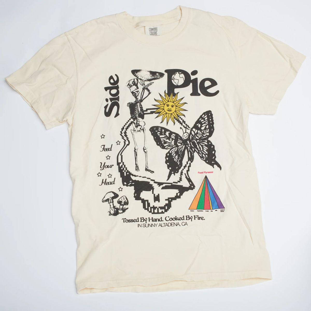 A white t-shirt with a prism, butterfly, yellow sun, and skeleton wearing a chef’s hat.