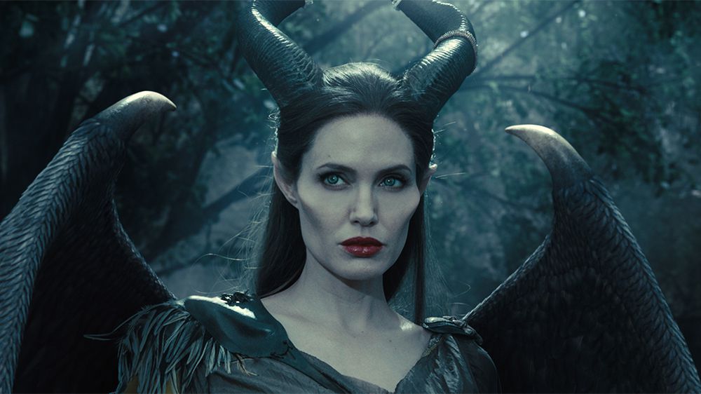 Maleficent (Angelina Jolie), with wings, horns, and enhanced cheekbones, looks wary in closeup in 2014’s Maleficent