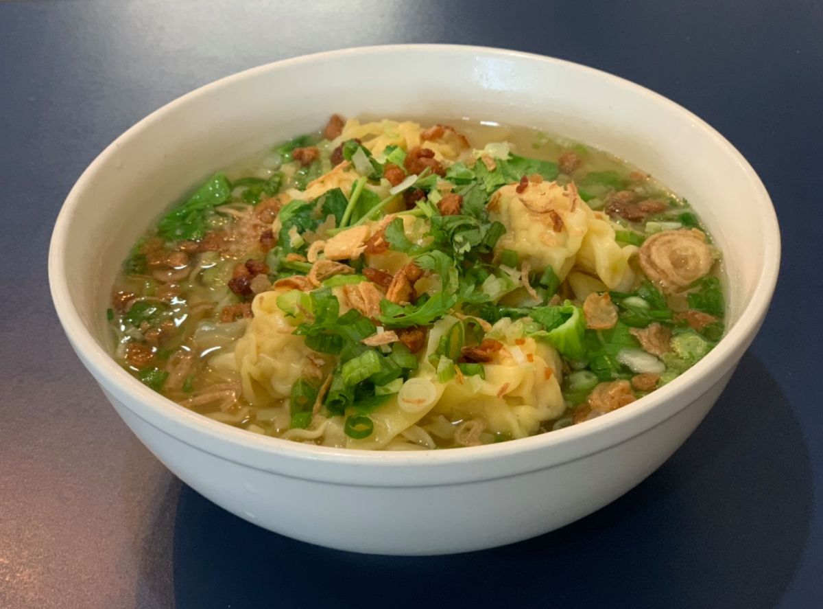 A bowl of soup with wontons and chopped vegetables peeking out