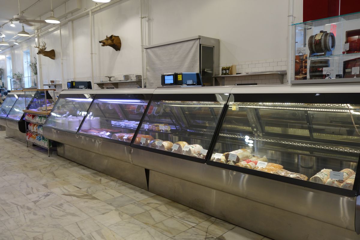 A nearly empty deli counter with a few hams sitting in a cold case
