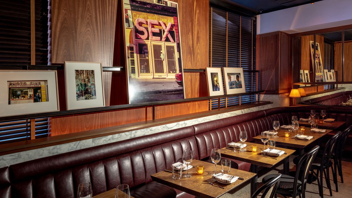 Framed photos lean against a wooden wall with a long leather banquette positioned beneath the artwork.