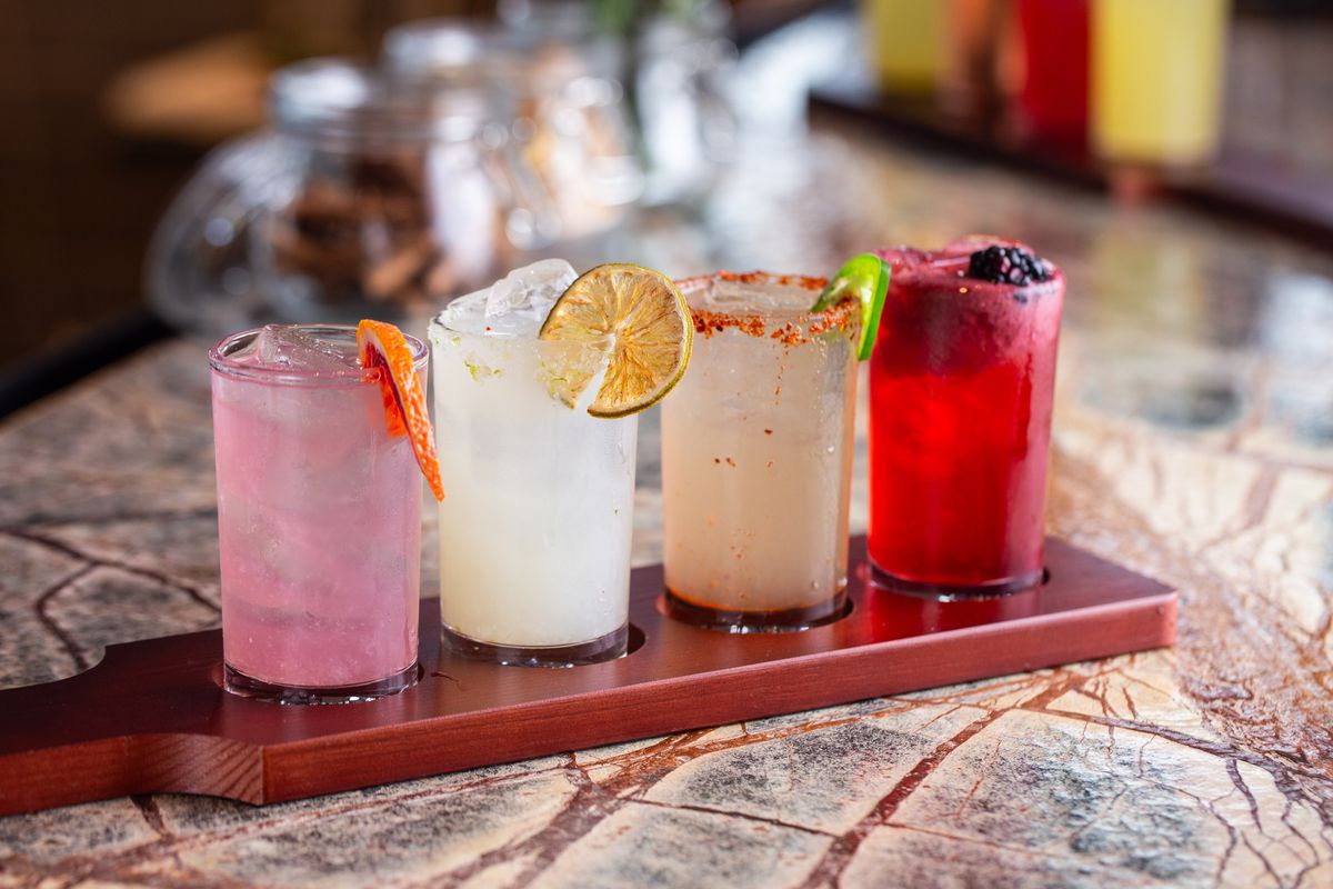 A flight of four margaritas on a wooden paddle placed atop a marble tabletop.