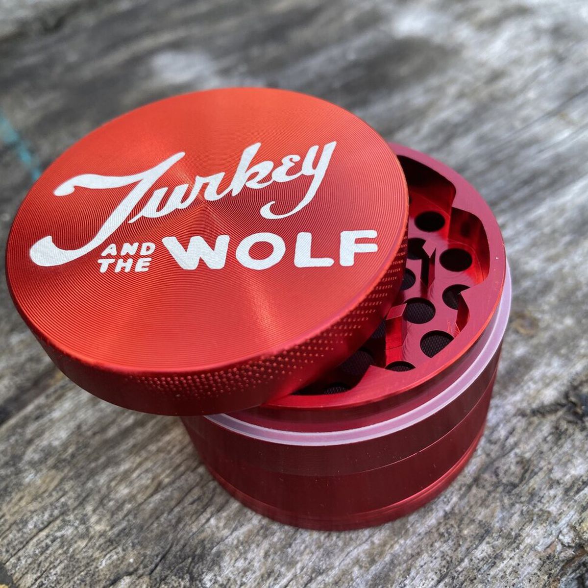 A red herb grinder with a Turkey and the Wolf logo